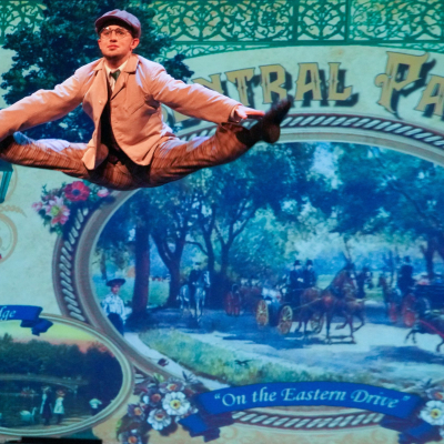 Hello Dolly ensemble dancer in a period suit performing in front of a Central Park backdrop