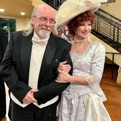 Hello Dolly performers in black formalwear and a white-and-silver period dress with a large hat